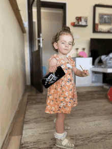 a little girl in a floral dress is holding a black bottle with a picture of a pirate on it