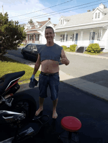 a man wearing a crop top stands in front of a motorcycle