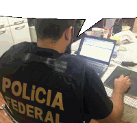 a man wearing a black vest that says policia federal sits in front of a laptop computer