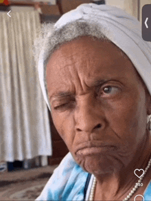 an older woman wearing a white head scarf and pearls making a funny face