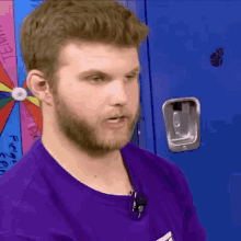 a man in a purple shirt is standing in front of a blue locker with a spinning wheel on it