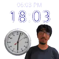 a man wearing glasses stands next to a clock that reads 1803