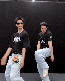 two young men are dancing in front of a black wall and one of them is wearing a shirt that says ' nc '