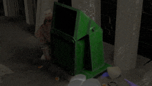 a green box with a black screen sits on the ground in a dark room