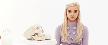 a blonde woman in a purple sweater is standing next to a skull