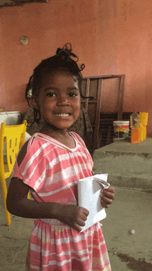 a young girl in a pink and white striped dress holds a piece of paper