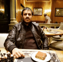 a man in a leather jacket sits at a table with a piece of cake on a plate