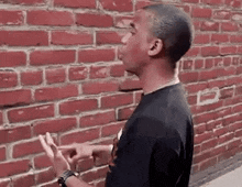 a man in a black shirt is standing in front of a brick wall .