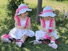 two little girls wearing matching dresses and hats are sitting on the grass