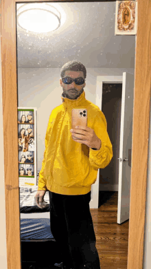 a man wearing sunglasses and a yellow jacket takes a picture of himself in a mirror