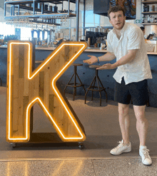 a man stands in front of a large neon k sign