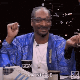 snoop dogg is sitting at a table with a cup of coffee and a cigarette .