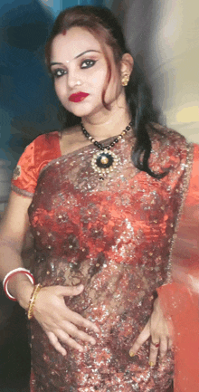 a woman wearing a red top and a necklace holds her hands on her hips