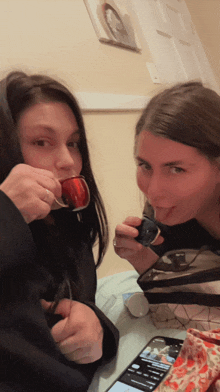 a woman drinking from a cup next to another woman drinking from a cup