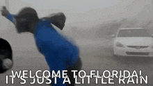 a man in a blue shirt is jumping in the air in front of a car in the rain .