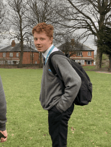 a boy with red hair wearing a grey sweater and black pants