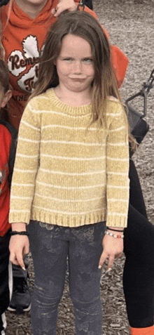 a girl wearing a yellow and white striped sweater is standing in a group of children