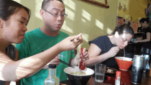 a man and two women are eating noodles in a restaurant