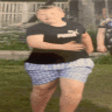 a young girl in a black puma shirt and blue shorts is standing in a field .