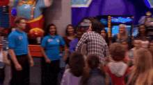 a man in a plaid shirt stands in front of a crowd of people in front of a clock that reads 07.00