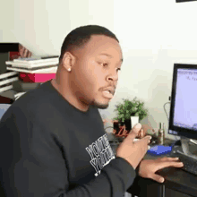 a man is sitting at a desk in front of a computer holding a cell phone in his hand .