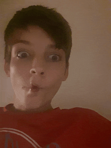 a young boy making a funny face with his mouth open wearing a red shirt