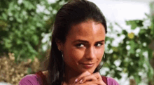 a close up of a woman 's face with her hands folded and a smile on her face .