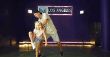 a man and a little girl are dancing on a stage in front of a sign that says los angeles .