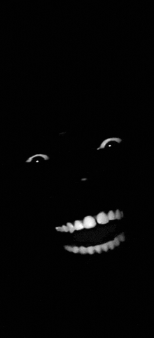 a black and white photo of a smiling face in the dark