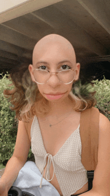 a woman with glasses and a shaved head looks at the camera