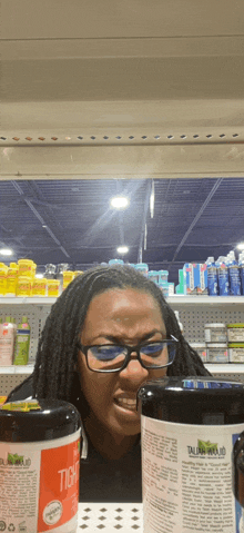 a woman wearing glasses is standing in front of a shelf with a jar that says " tic " on it