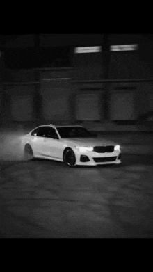 a black and white photo of a white bmw drifting on a wet road .