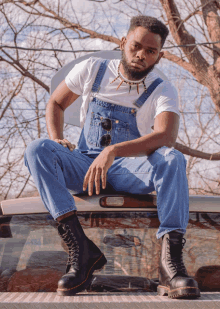 a man wearing overalls and boots sits on the back of a truck