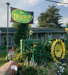 a green john deere tractor with a trump flag in front of a house