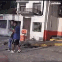 a man in a blue shirt is walking down a street in front of a building with red and white paint .