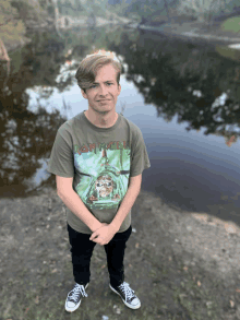 a young man wearing an iron maiden t-shirt stands in front of a body of water