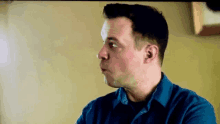 a man in a blue shirt is making a funny face while looking at something .