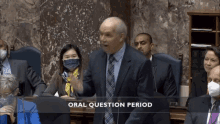 a man in a suit and tie is speaking in front of a group of people and the words oral question period are above him