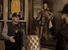 a man wearing a la jacket stands in front of a painting of a man