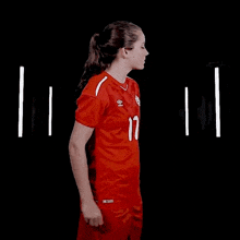 a woman in a red soccer uniform is standing in a dark room .