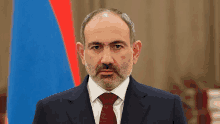 a man in a suit and tie is standing in front of a blue and red flag