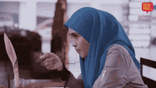 a woman in a hijab is sitting at a table with a spoon in her mouth