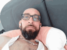 a bald man with glasses and a beard is laying on a couch