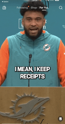 a man wearing a miami dolphins jacket stands at a podium