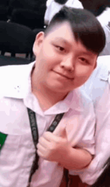 a young boy in a white shirt is giving a thumbs up and smiling .