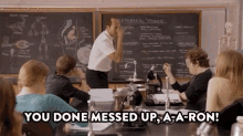 a man is standing in front of a blackboard in a classroom with a group of students sitting at desks .