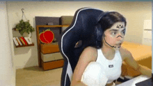 a woman wearing headphones and a white tank top is sitting in a chair with a face drawn on her face .