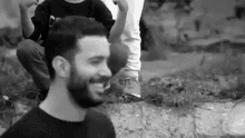 a black and white photo of a man with a beard smiling while sitting on the ground .