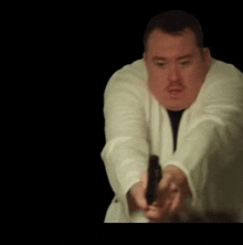 a man in a white robe is pointing a gun at someone .