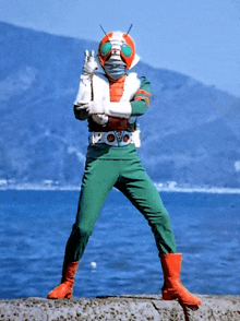 a man in a superhero costume stands in front of a body of water with mountains in the background